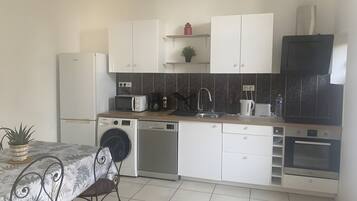 Una cocina compacta con gabinetes blancos, microondas, cafetera y lavavajillas.
