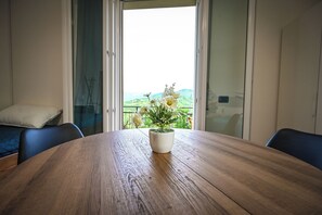 Ett träbord med en krukväxt i mitten, en soffa och en utsikt över grönskan genom en glasdörr.