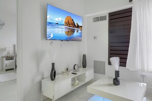 A modern bathroom with a large mirror, a vanity with a sink, and a television mounted on the wall displaying a beach scene. - Prime Location,  2 Queen, Near Universal (Orlando)