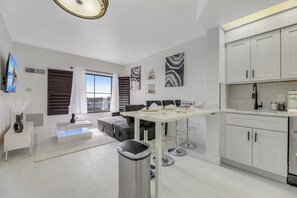 A modern kitchen with white cabinets, a dining area with a table and chairs, and a large window with curtains. - Prime Location,  2 Queen, Near Universal (Orlando)