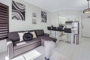 A modern living room with a grey sofa, black and white abstract paintings, and a kitchen in the background. - Prime Location,  2 Queen, Near Universal (Orlando)