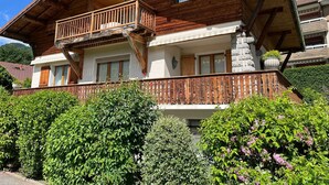 A two-story wooden chalet with a balcony, stone facade, and lush greenery. - Charming, fully equipped apartment in a chalet for a couple, with a panoramic view (sallanches)
