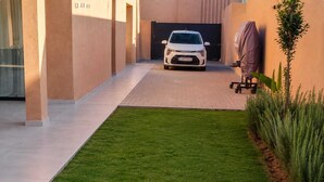 A car parked in a driveway with a lawn and plants on the side.