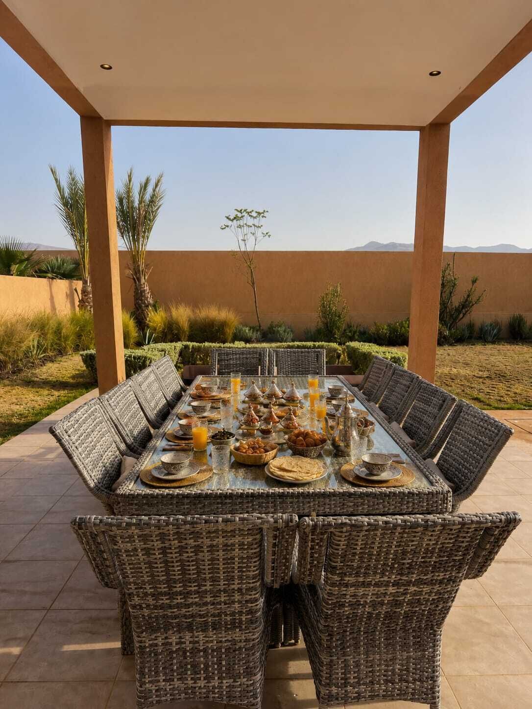 Un espace de restauration en plein air avec une table dressée pour un repas, entourée de chaises en osier.