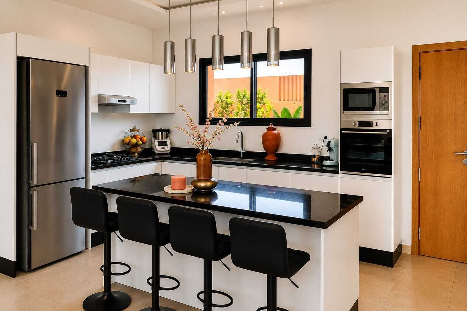 Une cuisine moderne dotée d’un îlot central, de tabourets de bar, d’appareils électroménagers en acier inoxydable et de luminaires suspendus.