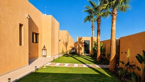 A courtyard with palm trees, a pathway, and a building with a flat roof.