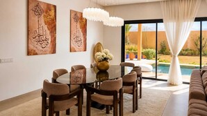 A modern dining area with a glass table surrounded by chairs, a chandelier, and artwork on the walls.