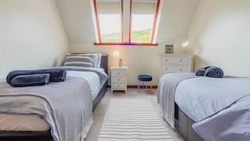 A bedroom with two beds, a nightstand, a dresser, and a window with a view.