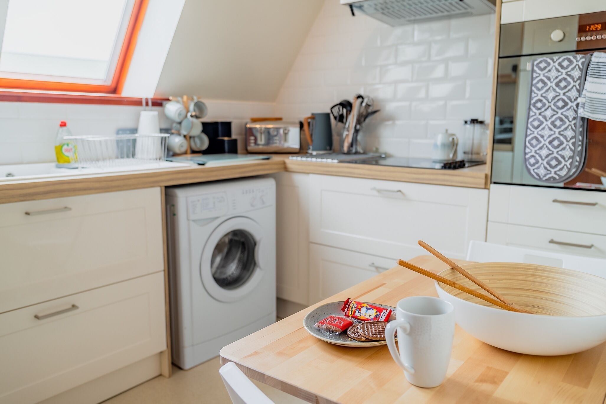 A modern kitchen with a washing machine, wooden countertop, and a bowl with chopsticks.