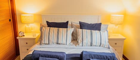 A neatly made bed with striped bedding and multiple pillows, flanked by bedside tables with lamps and a clock.