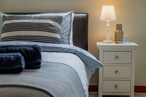 A neatly made bed with striped bedding and a pillow, a bedside lamp, a glass of water, and a white nightstand with drawers.