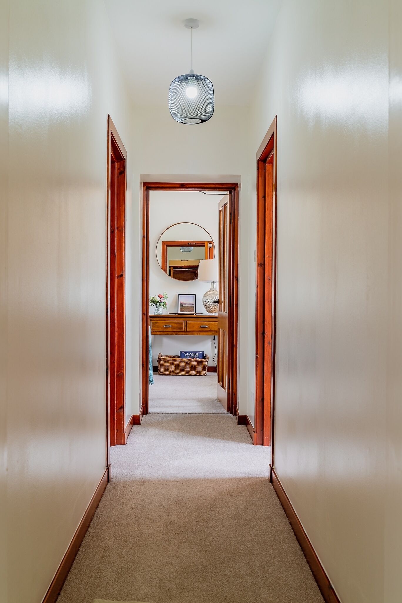 A hallway with a wooden door frame, a hanging light fixture, a mirror, and a small table with a lamp.