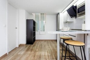 Eine kleine Küche mit weißer Arbeitsplatte, zwei Holzhockern und einem schwarzen Schrank.