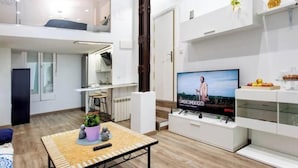 Una sala de estar moderna con televisor de pantalla plana, una zona de comedor y una escalera que conduce a un nivel superior.