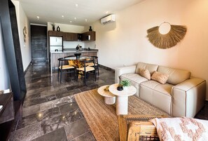 A modern living room with a sofa, a coffee table, and a dining area with chairs. - Luxury 3BR Tulum Penthouse with Private Pool (Tulum)