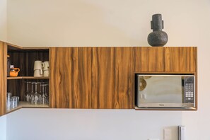 A kitchen with wooden cabinetry, a microwave, and a shelf with cups and glasses. - Luxury 3BR Tulum Penthouse with Private Pool (Tulum)
