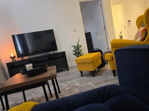 A living room with a flat-screen TV, a coffee table, yellow armchairs, and a dark sofa. - Solihull - 10 mins to NEC & Airport. Free Parking (Solihull)