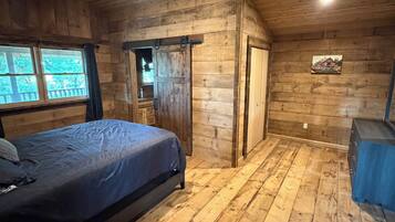 A wooden cabin bedroom with a bed, a ceiling fan, a window, and a door.