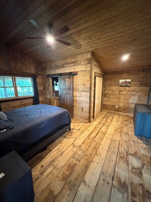 Un dormitorio de cabaña de madera con una cama, un ventilador de techo, una ventana y una puerta.