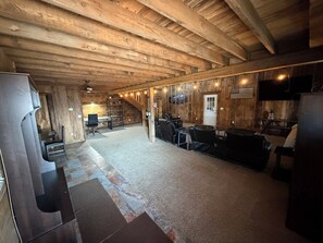 A spacious room with a wooden ceiling, a seating area with chairs, a television, and a door with an American flag.