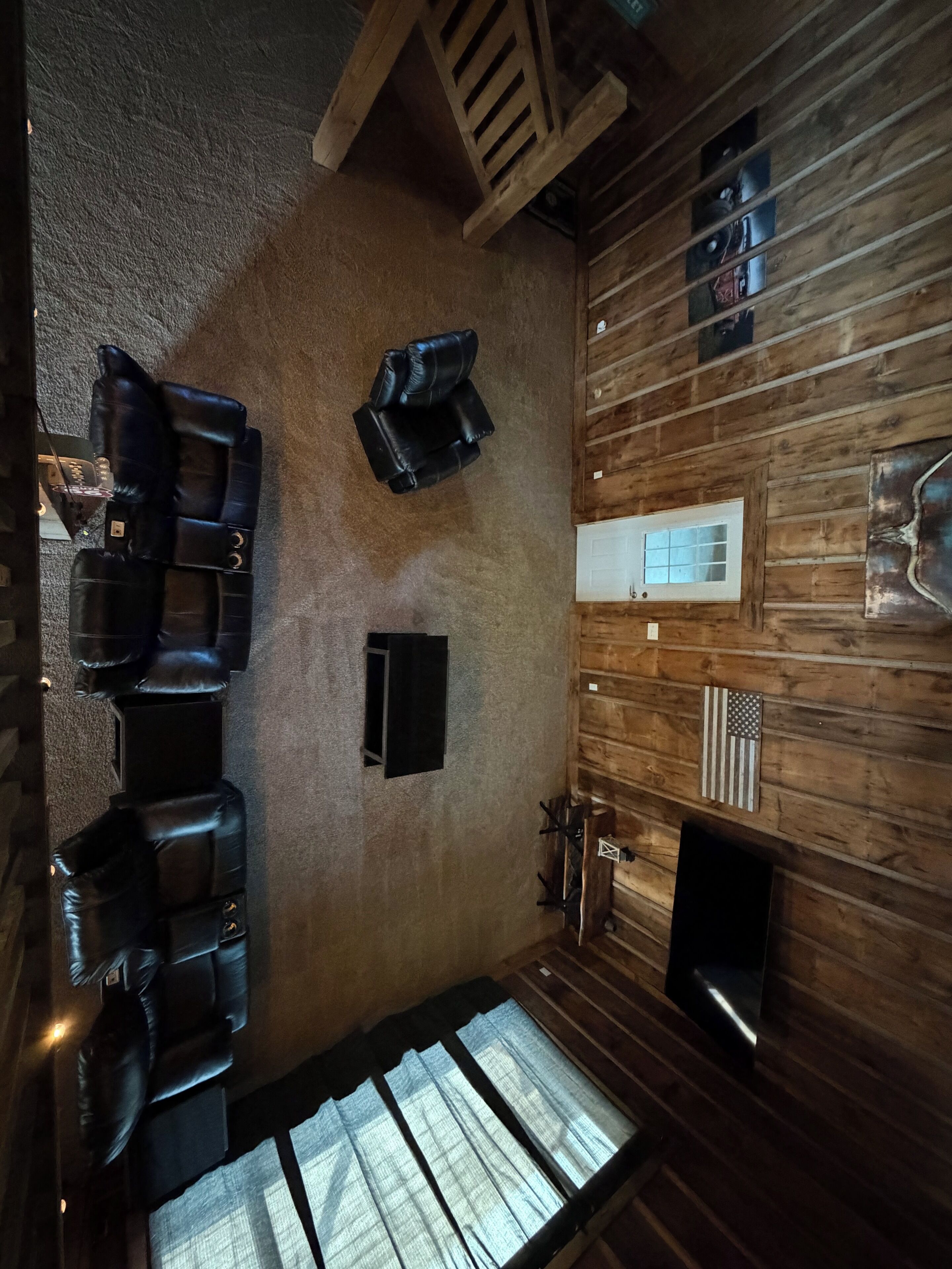 A room with a sloped ceiling, wooden walls, a fireplace, and a seating area with black leather chairs.