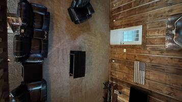 A room with a sloped ceiling, wooden walls, a fireplace, and a seating area with black leather chairs.