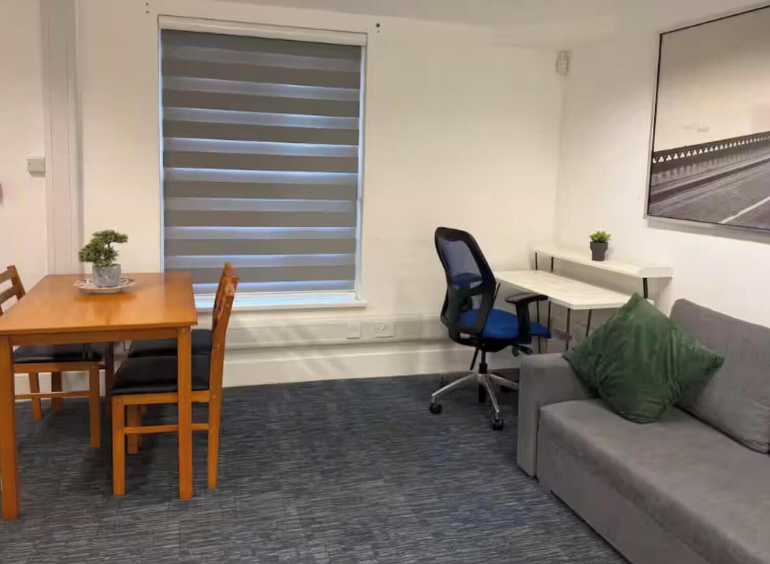 A room with a dining table, chairs, a sofa, a desk, and a window with blinds.