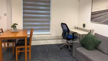 A room with a dining table, chairs, a sofa, a desk, and a window with blinds.