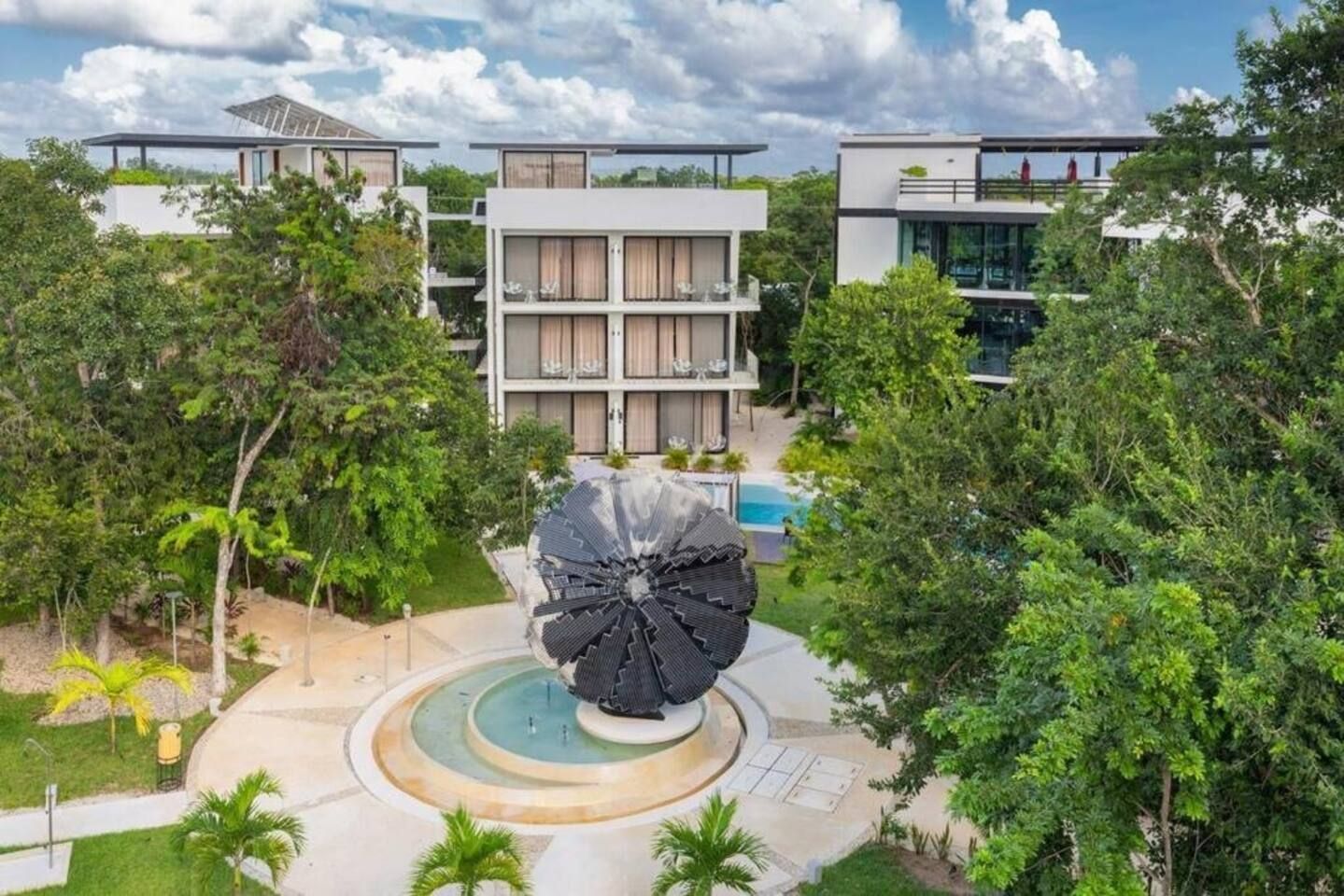A modern hotel with a central courtyard, a large water feature, and lush greenery.