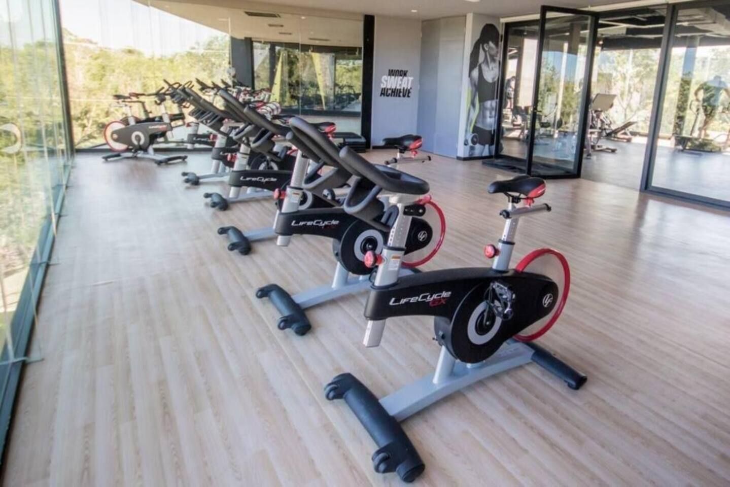 A gym with multiple stationary bikes, a motivational poster, and a view through large windows.
