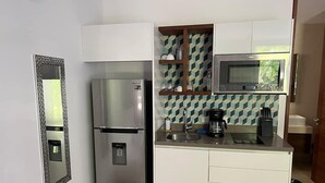 Una cocina funcional con refrigerador, microondas y cafetera sobre la encimera.