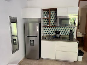 Eine kleine Küche mit Kühlschrank, Mikrowelle und einer Kaffeemaschine auf der Arbeitsplatte.