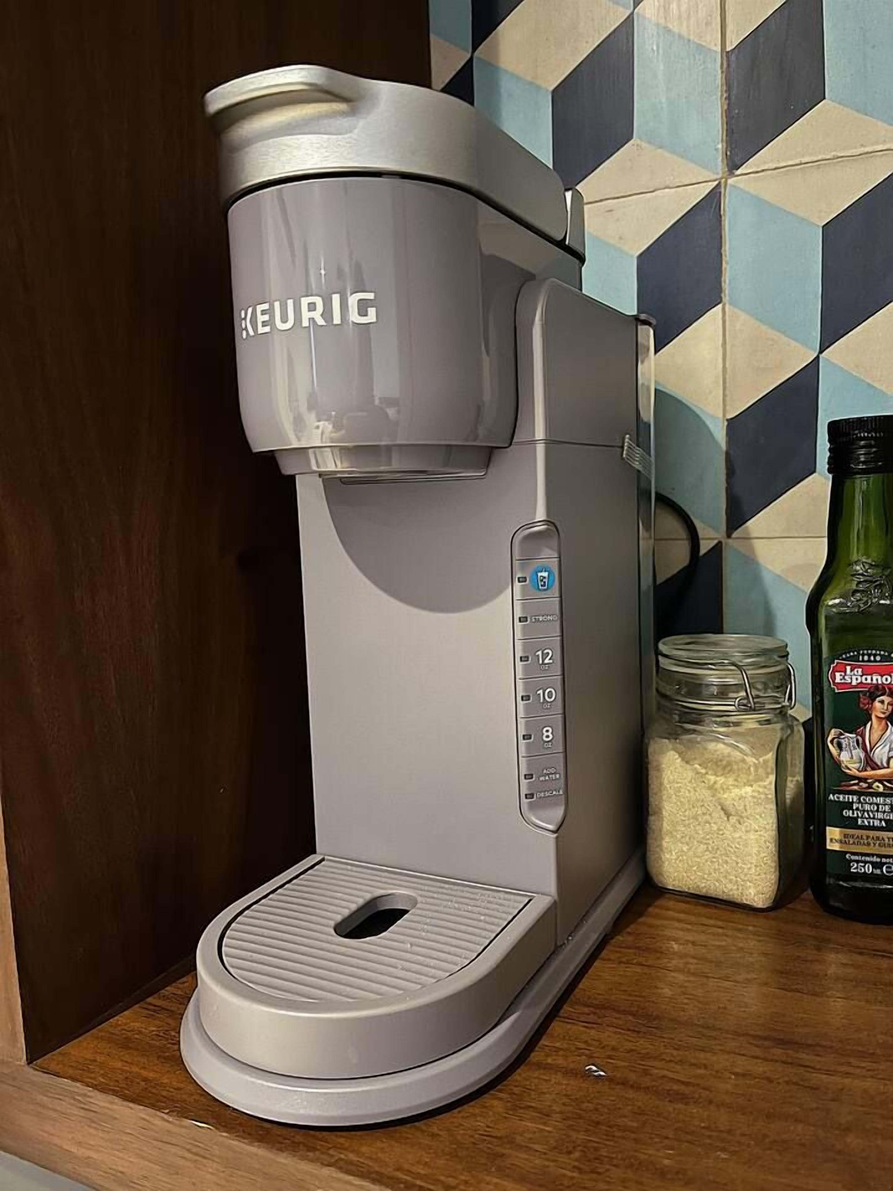 A Keurig coffee maker with a control panel, a jar of coffee grounds, and a bottle of olive oil on a wooden surface.
