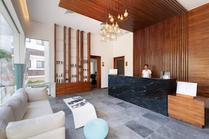 Ein Hotel-Rezeptionsbereich mit einer Marmor-Theke, Holzvertäfelung, einer Kristallleuchtre und einem Sofa.