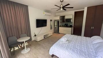 A hotel room with a bed, a desk, a chair, a television, an air conditioning unit, and a kitchenette.