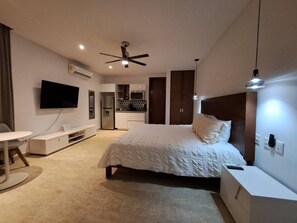 Une chambre d’hôtel moderne équipée d’un lit, d’une table de chevet, d’une télévision et d’un coin cuisine.
