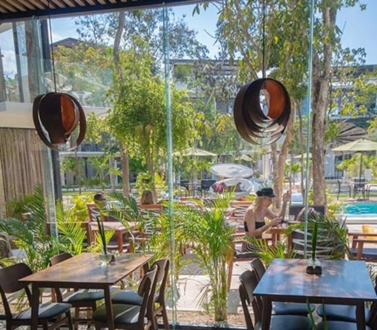 An outdoor dining area with tables and chairs, surrounded by greenery and a pool.