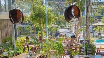 An outdoor dining area with tables and chairs, surrounded by greenery and a pool.