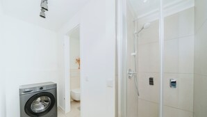 Moderni kylpyhuone, jossa on pesukone, wc ja lasiseinällä varustettu suihku.