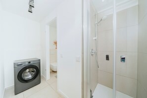 Un bagno moderno con lavatrice, WC e cabina doccia in vetro.