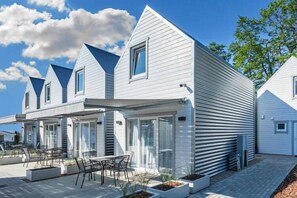 Ein modernes, zweigeschossiges Haus mit überdachter Terrasse und Sitzbereich im Freien.