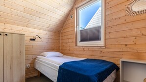 Pieni huone, jossa on yksi sänky, puupaneeliseinät, ikkunassa sälekaihtimet, yöpöytä ja vaatekaappi.
