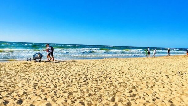 A sandy beach with people walking and a stroller in the foreground. - Comfortable holiday homes with SPA Rewal (Rewal)
