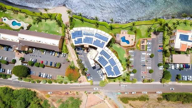 An aerial view of a coastal resort with a curved building, parking areas, and a beach. - Beachfront 4BR, 2 Condos for 12 in Maalaea! (Wailuku)