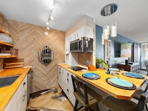 A modern kitchen with a herringbone floor pattern, wooden countertops, and a central island with blue placemats. - Maalaea, Island Sands, Spacious 4 BR, Beachfront, Sleeps 12 (Wailuku)