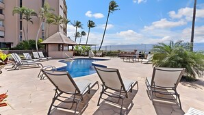 A pool area with lounge chairs, a small hut, and a view of mountains. - Beachfront 4BR, 2 Condos for 12 in Maalaea! (Wailuku)