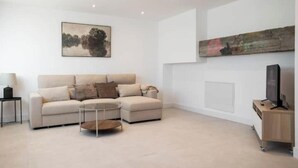 Ein modernes Wohnzimmer mit einem Ecksofa, einem Couchtisch, einem Flachbildfernseher und Kunstwerken an den Wänden.