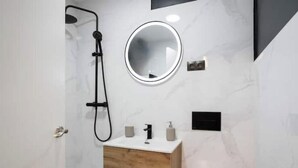 Ein modernes Badezimmer mit Dusche, rundem Spiegel, Holzwaschtisch und Toilette.