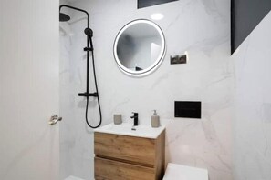 Ein modernes Badezimmer mit Dusche, rundem Spiegel, Holzwaschtisch und Toilette.