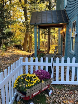 A wooden cart with flowers, a white picket fence, and a house with a porch.